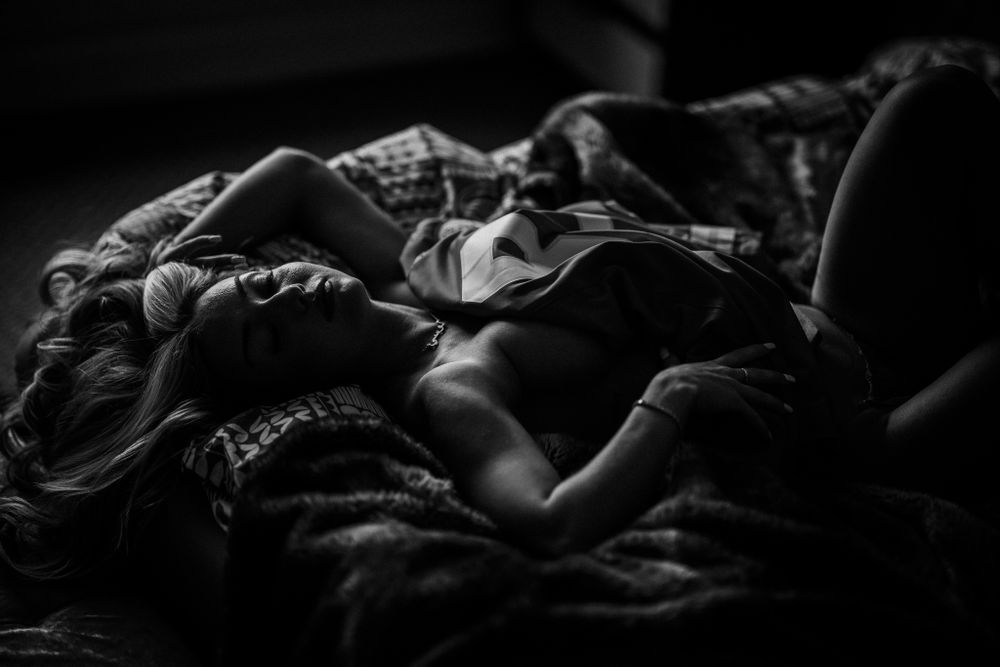 Dramatic monochrome photo of someone sleeping beneath textured blankets and shadows.