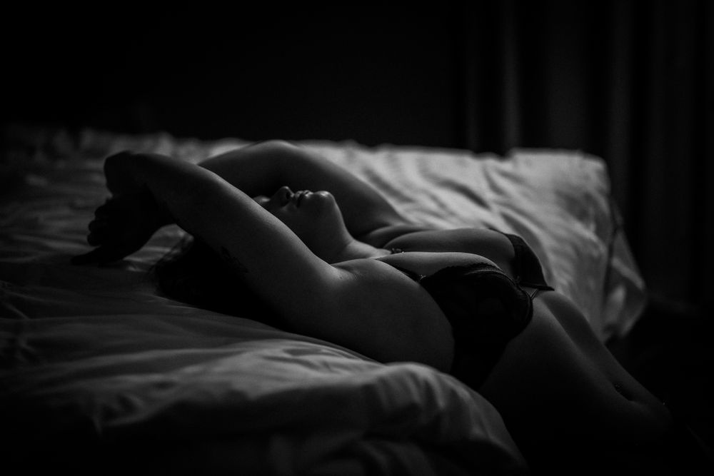 Dramatic monochrome photo of someone sleeping beneath textured blankets and shadows.