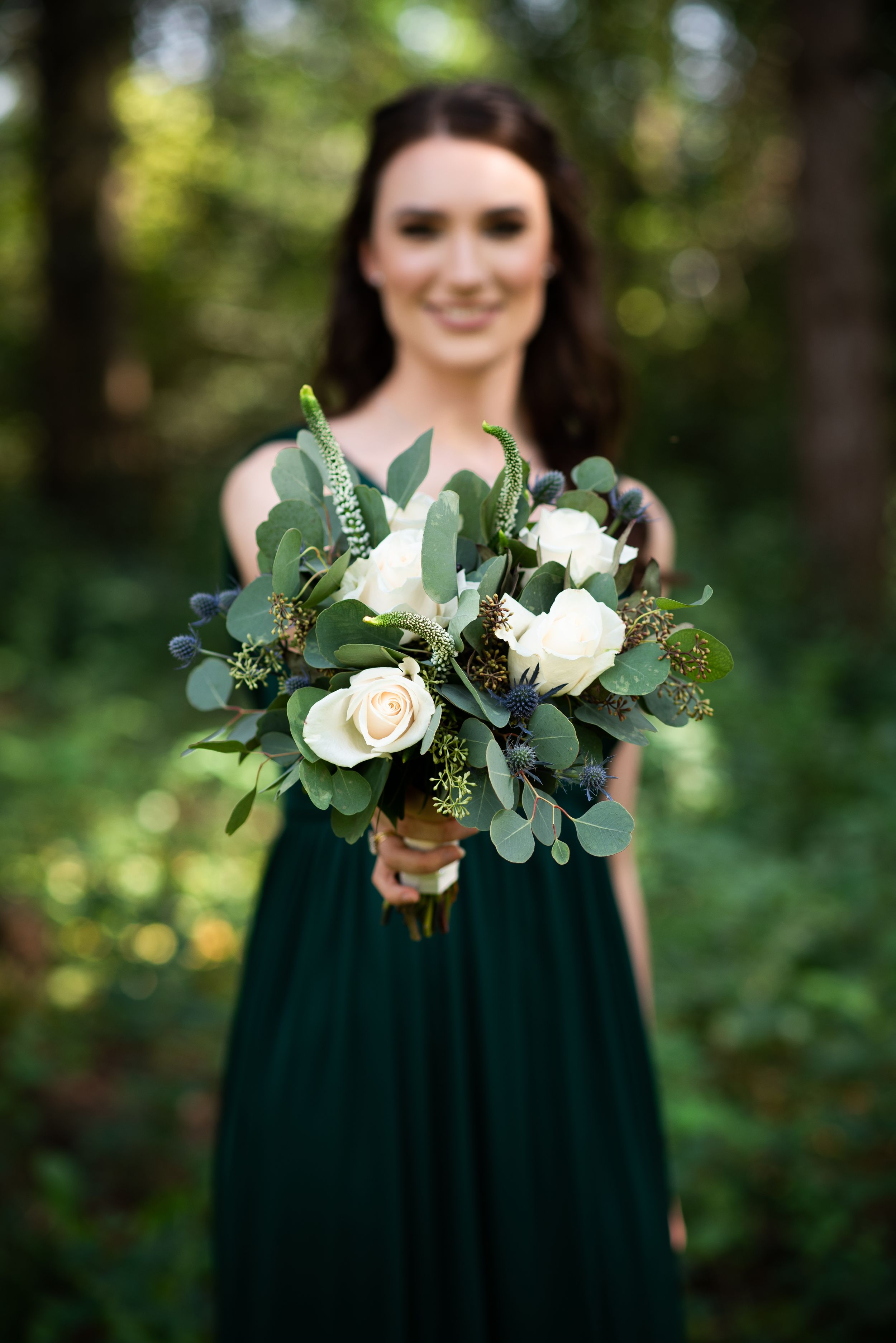 Elegant bouquet of white roses and eucalyptus leaves held against forest backdrop.