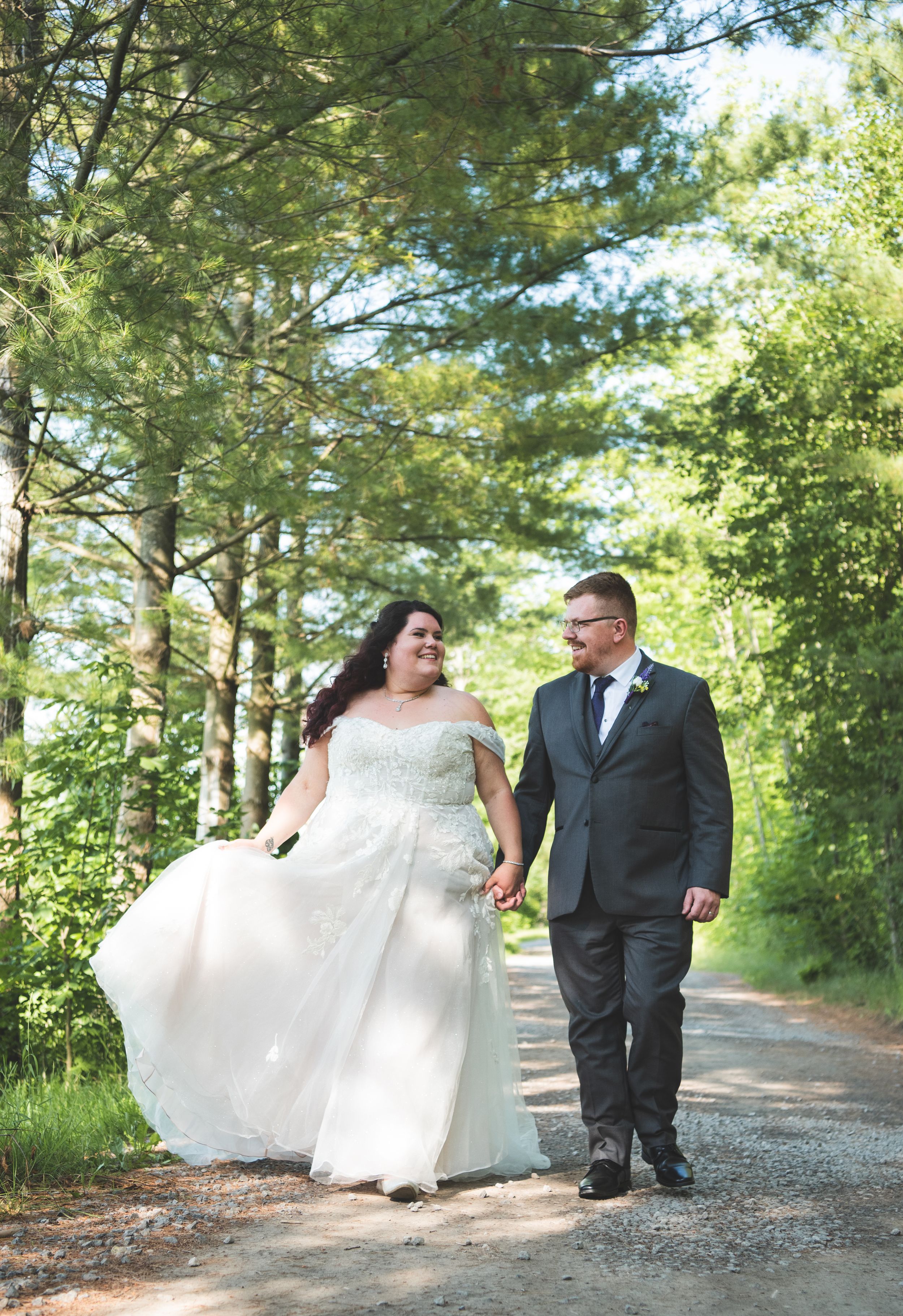 A couple walking together on a tree-lined path during their wedding day celebration.