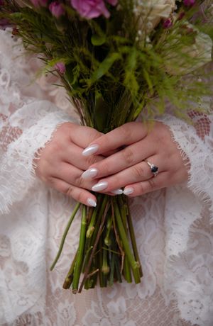 Close-up of hands holding a wedding bouquet against white lace fabric showing an engagement ring.