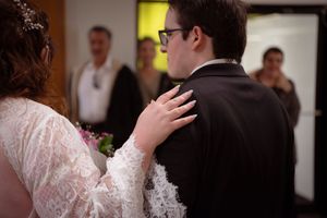 A tender moment at a wedding as a bride in lace touches her partner's shoulder during the ceremony.