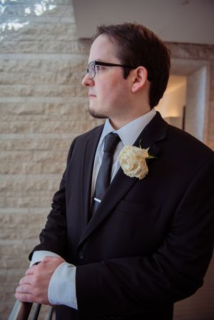 A person in a black suit and glasses gazes thoughtfully to the side in an elegant indoor setting.