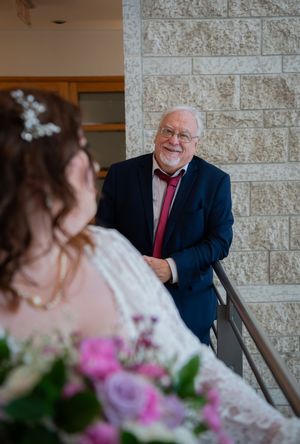 A heartwarming wedding moment captured in front of a stone wall with pink floral decorations in the foreground.