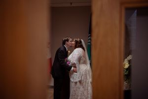 A couple stands together during an indoor wedding ceremony with warm lighting and wooden decor.