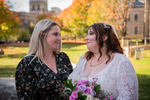 Autumn wedding scene outdoors with golden foliage and stone architecture in background.
