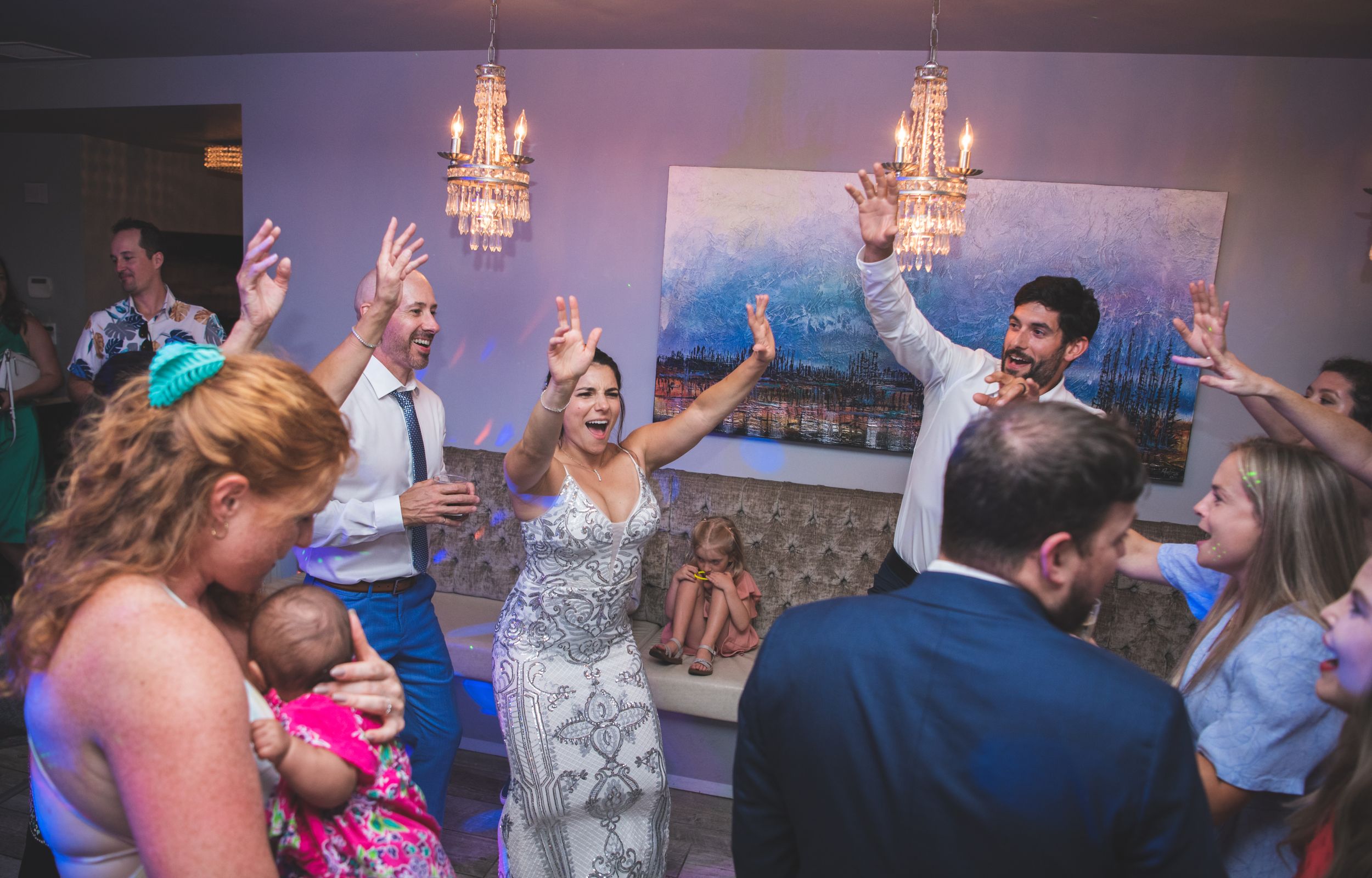 Wedding reception party scene with guests dancing under elegant chandeliers.