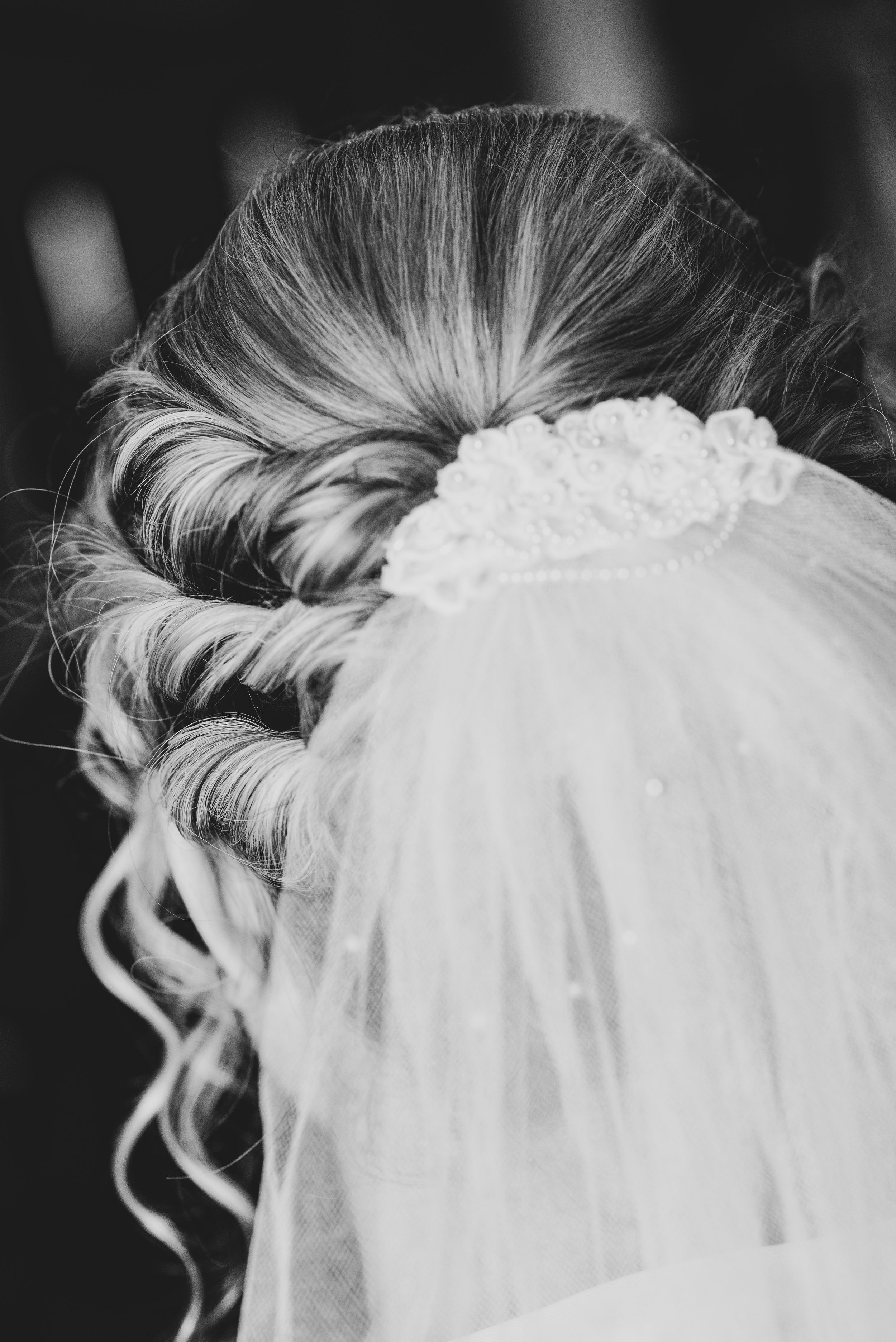 A close-up black and white photo of an elegant bridal updo with veil and floral details.