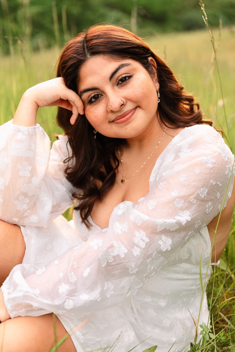 Outdoor portrait session in a grassy field wearing a white lace top with natural lighting.
