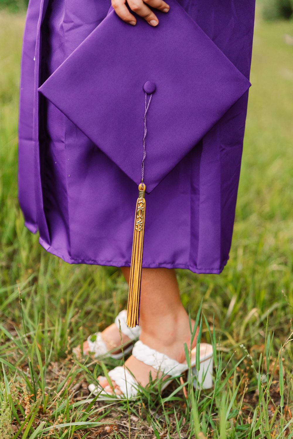 Detail shot of purple graduation gown and gold tassel against green grass.
