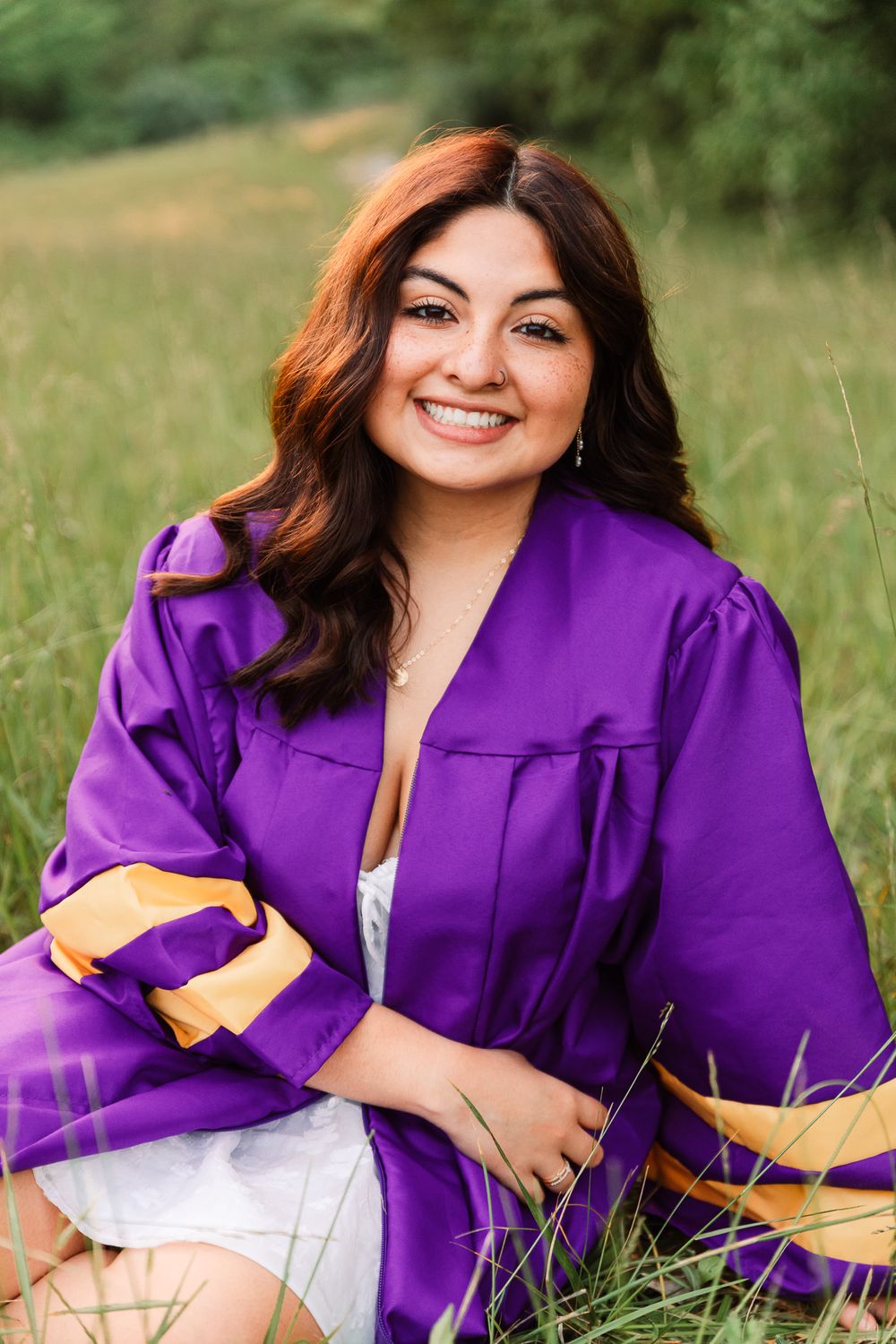 Graduate lying in grass wearing purple graduation gown during outdoor photo session.