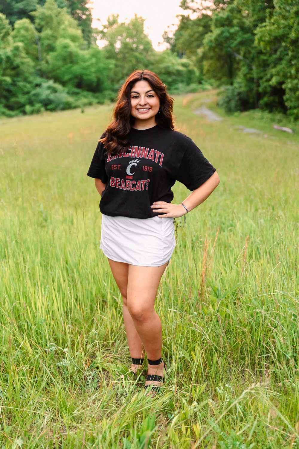 Person wearing University of Cincinnati t-shirt poses in tall grass field.
