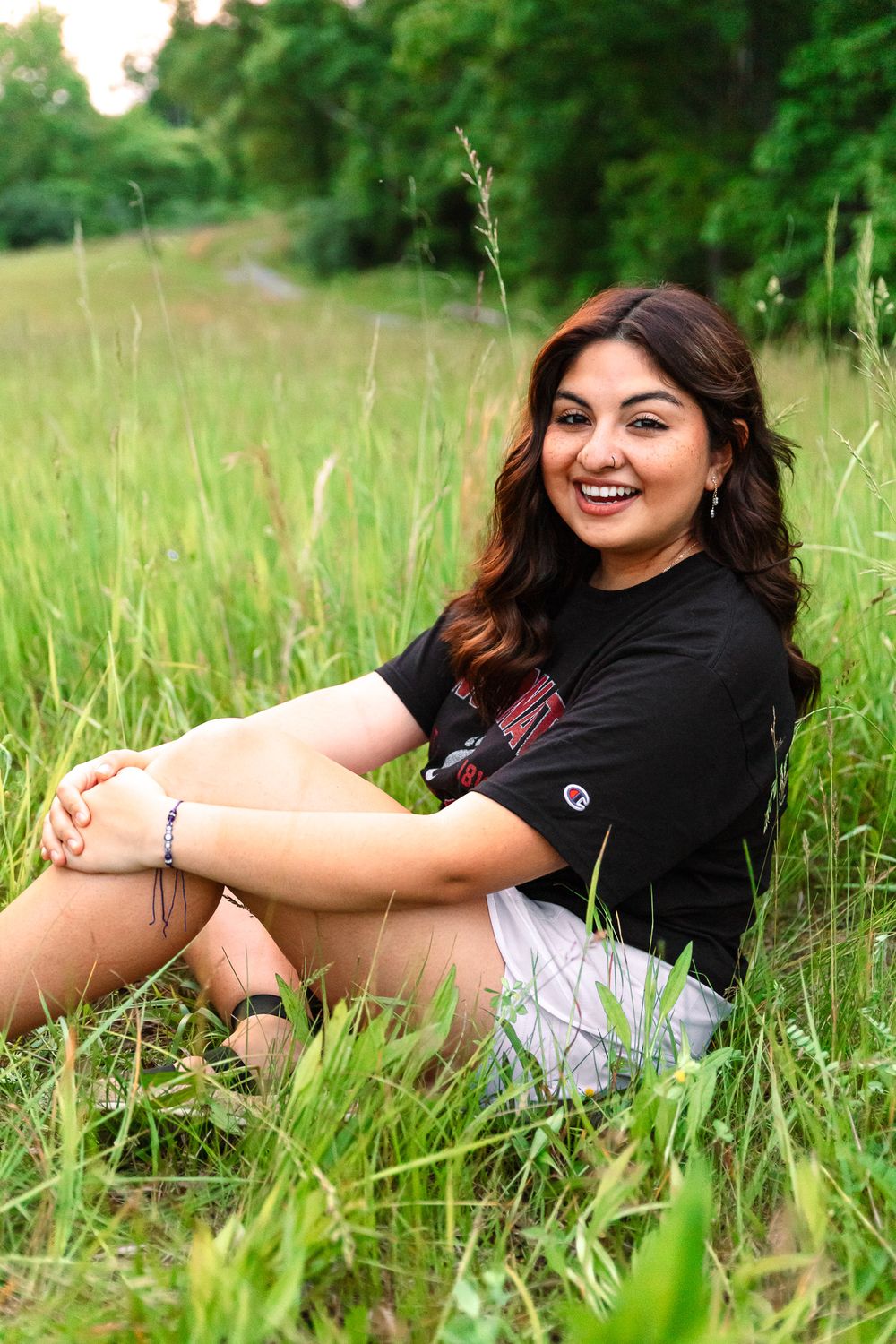 Portrait session in tall green grass wearing black shirt and white shorts on a sunny day.
