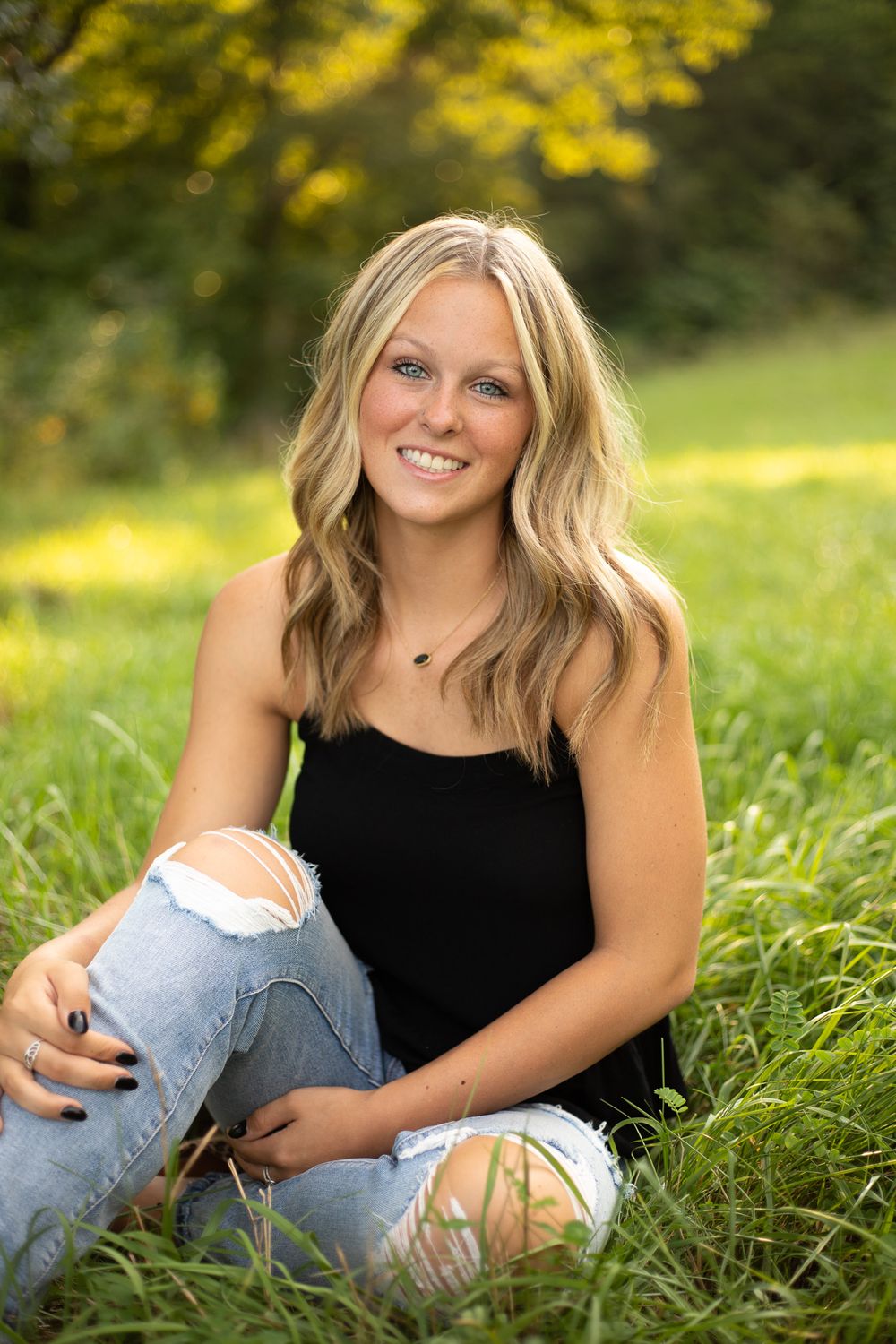 Senior portrait session in field wearing black top and distressed jeans.