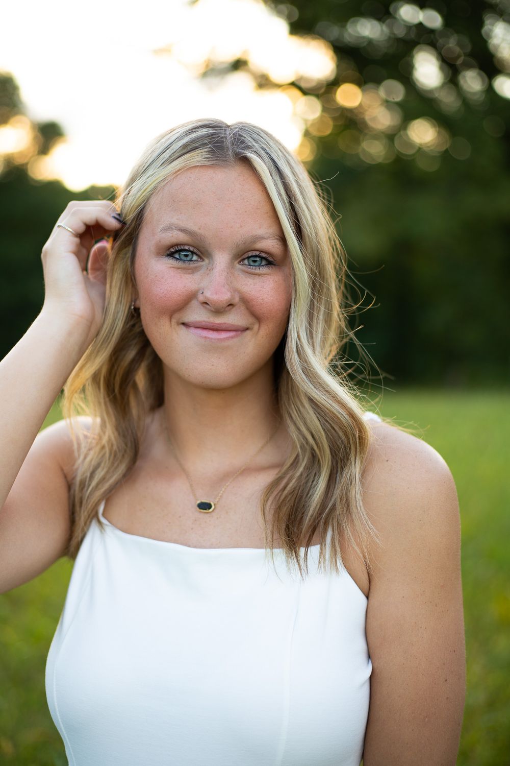 Summer portrait in white sleeveless top against natural outdoor backdrop.