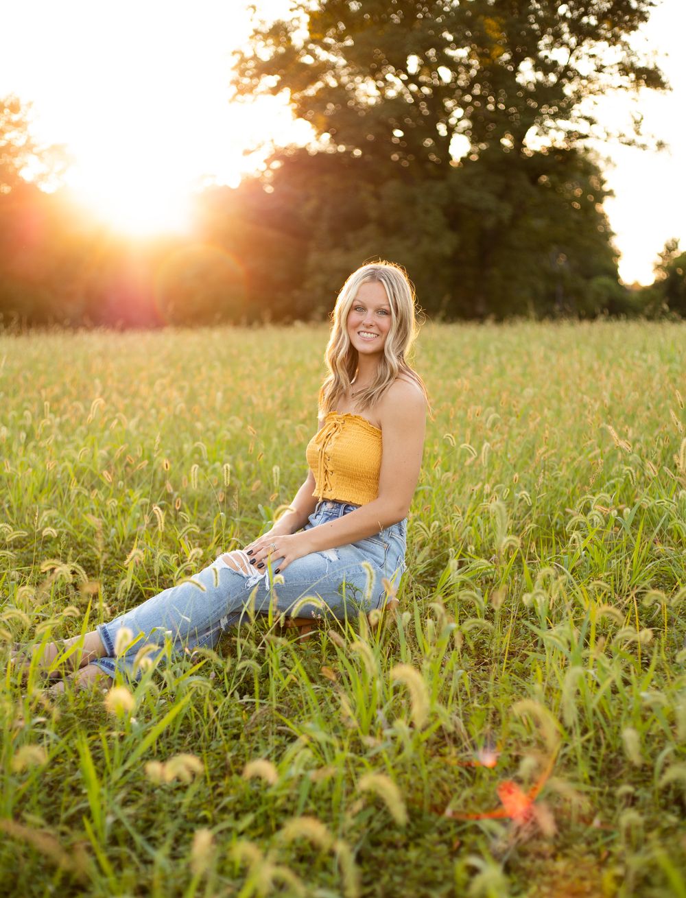 Golden hour portrait session in field wearing yellow top and jeans.