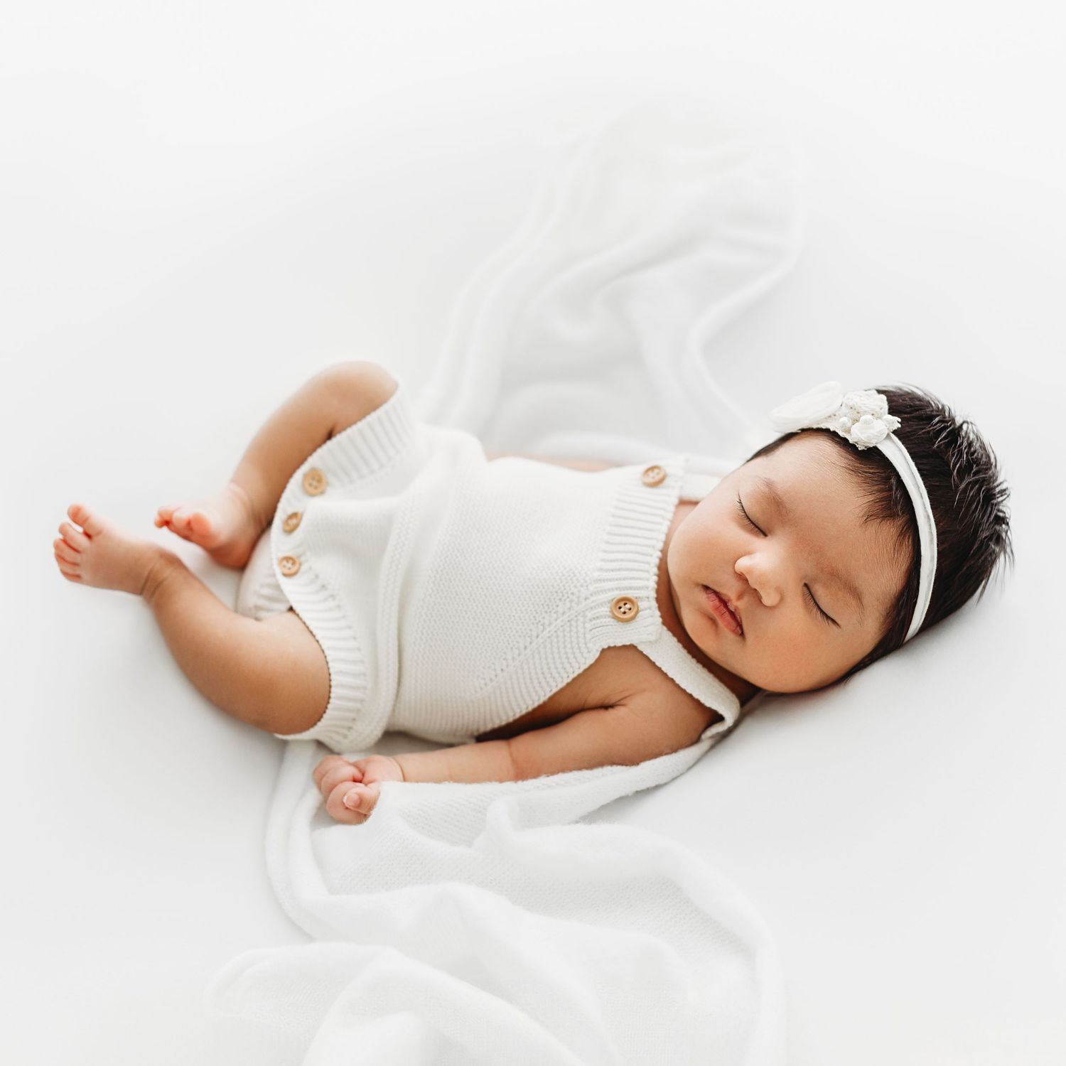 1 week old baby girl, with white blanket draped beside her, sleeping on her back on a white sheet