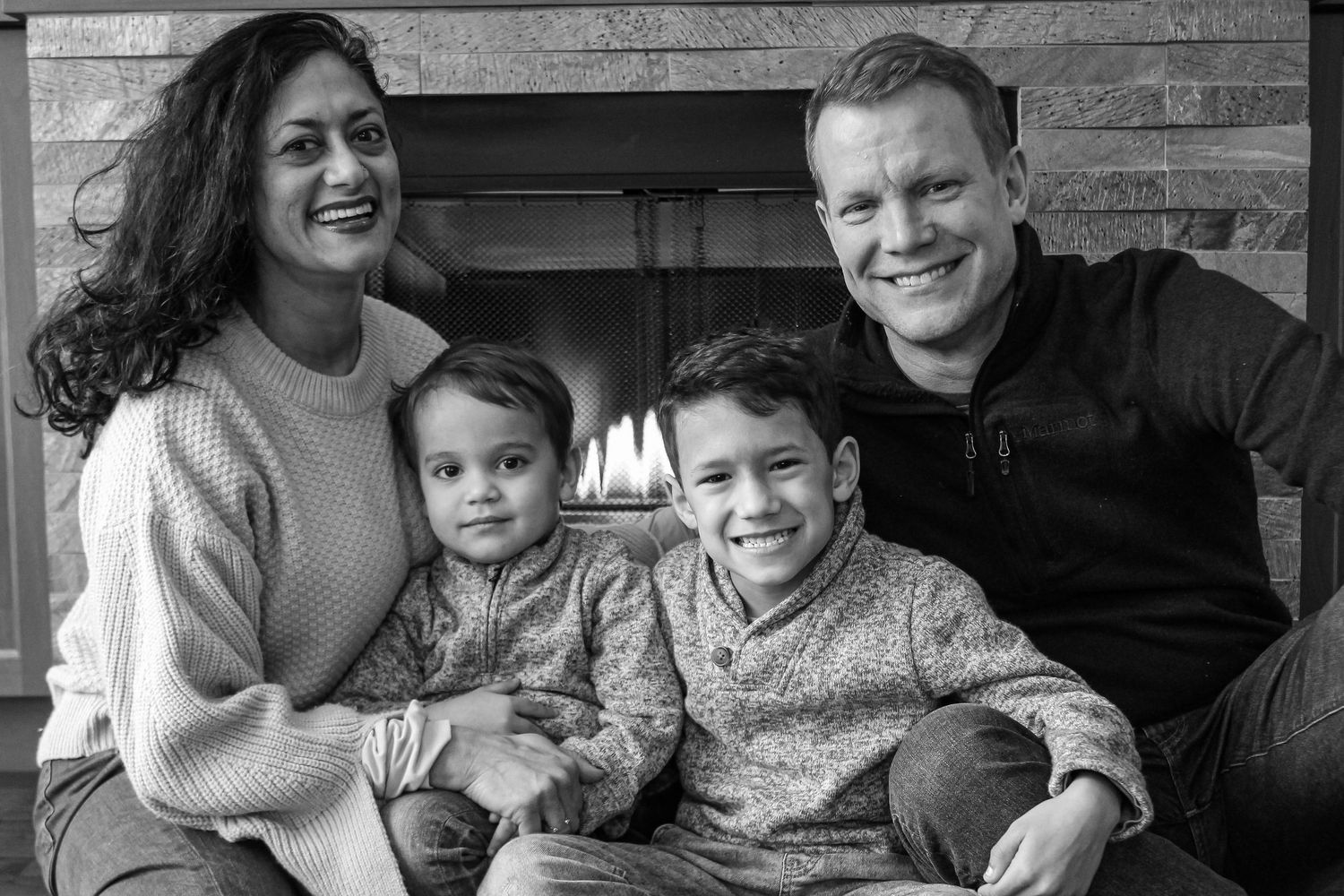 A family of four sits together on a wooden bench for a casual portrait.