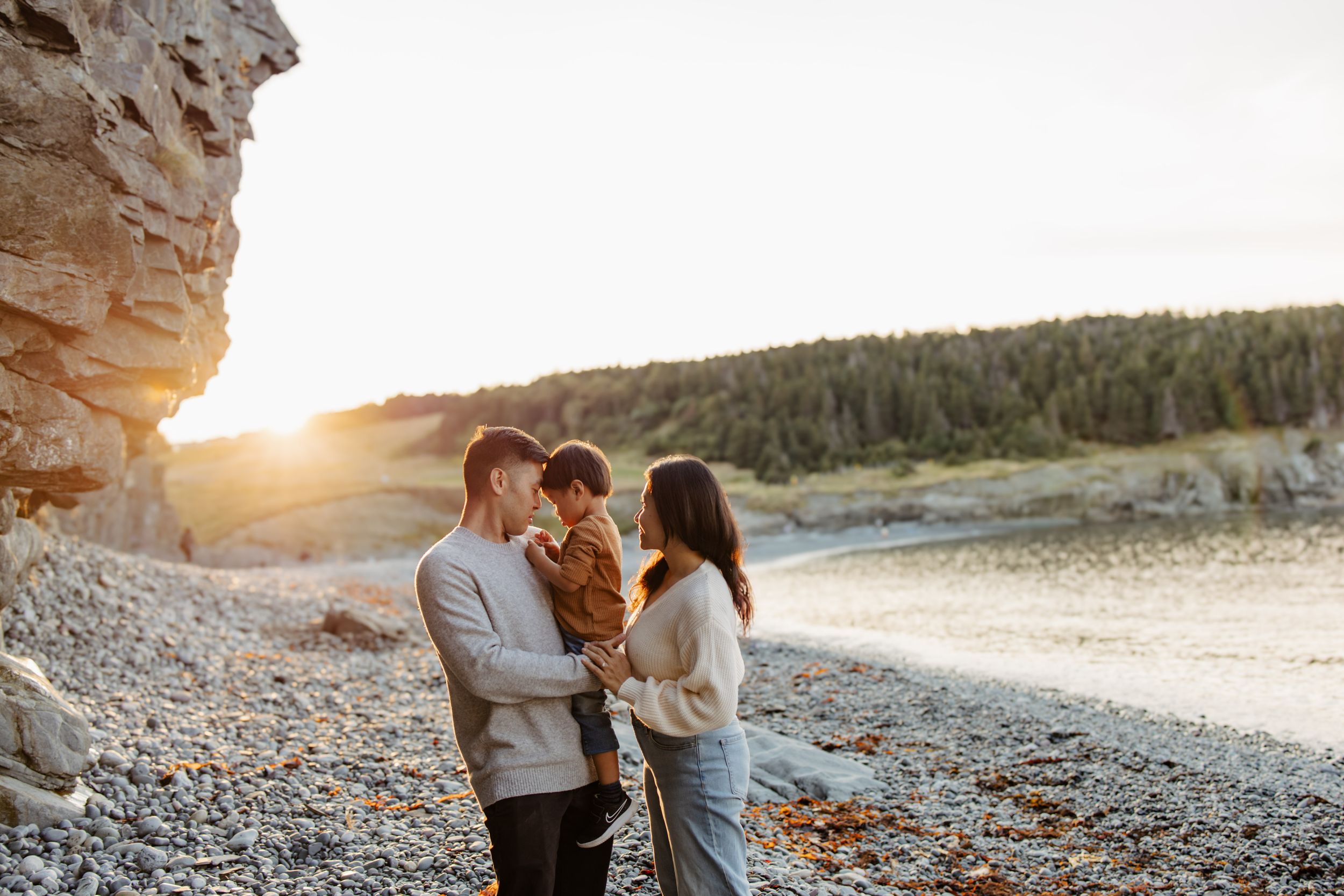 A couple embracing on a rocky beach at sunset with dramatic coastal cliffs.