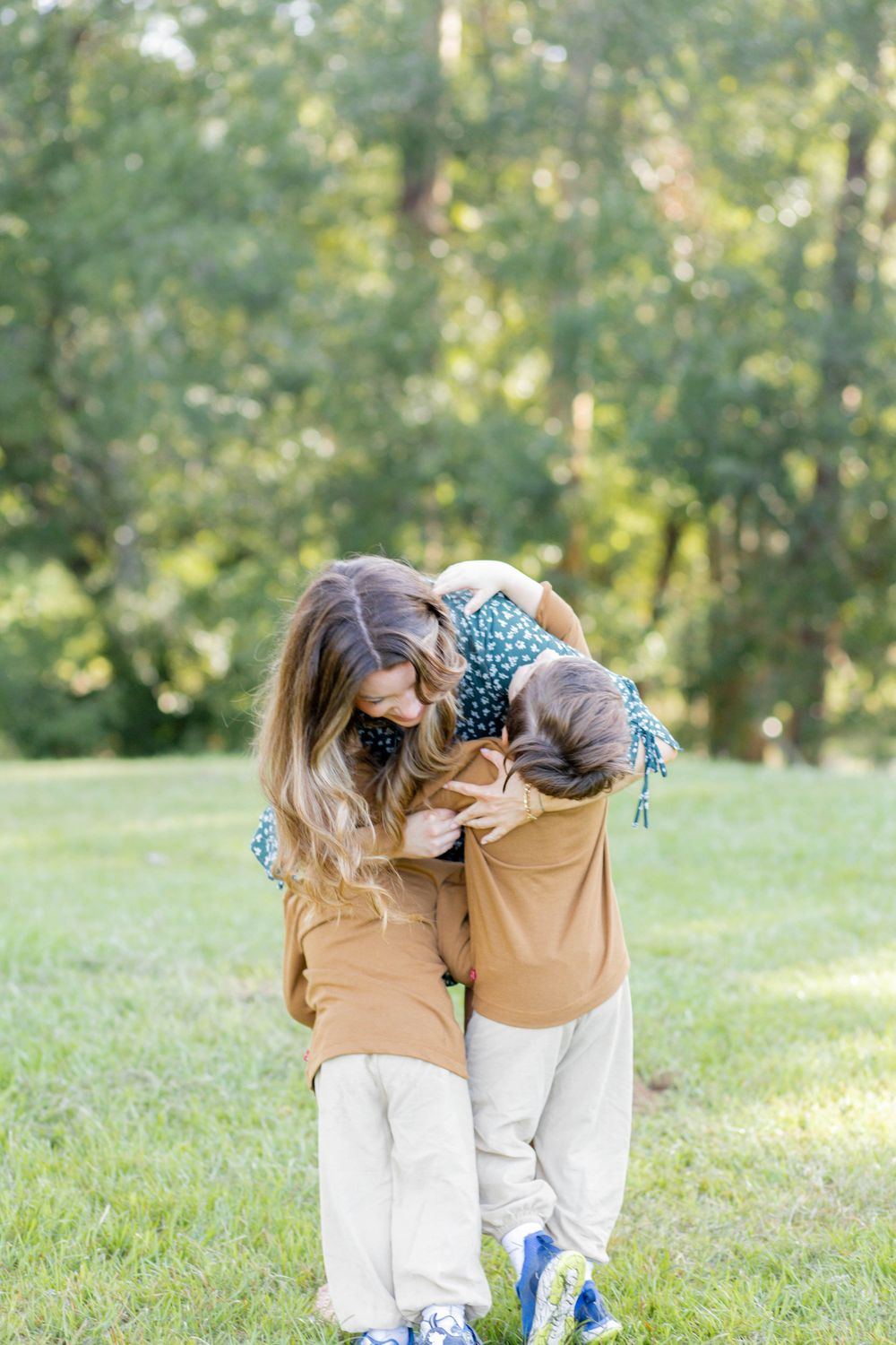 Two people in matching tan sweaters and white pants share an intimate moment in a sunny outdoor park setting.