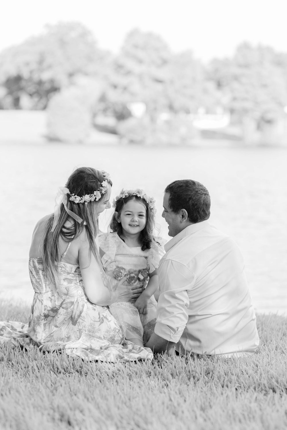Black and white photo of three people sitting together on grass having a tender moment.