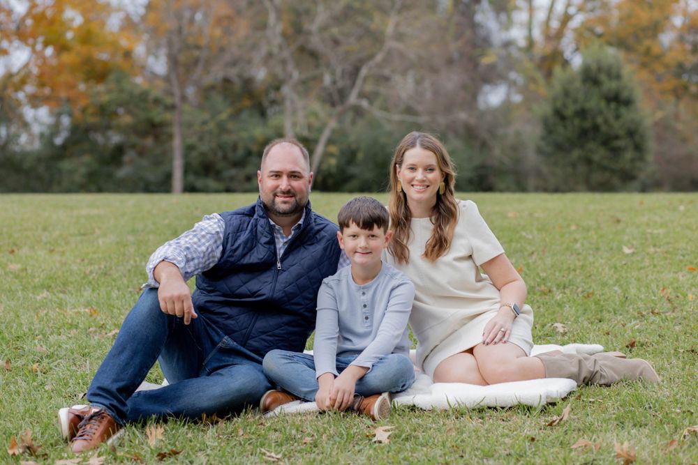 Family of three relaxes together on grass during autumn outdoor photo session.