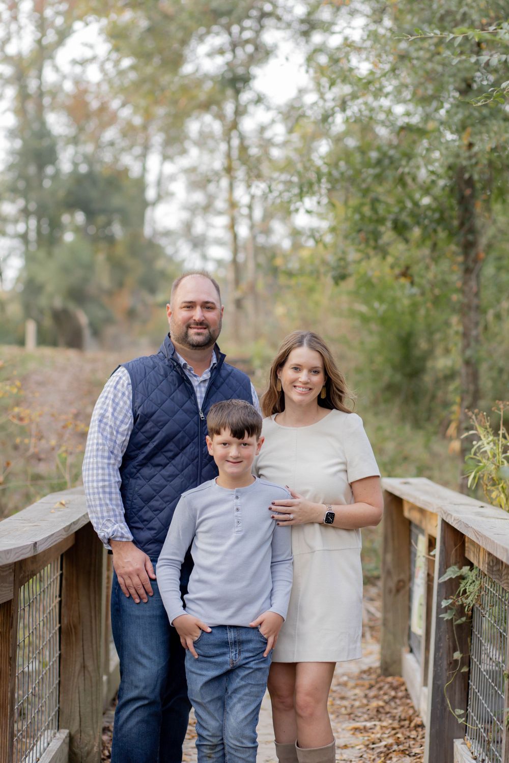 Family poses together on wooden bridge surrounded by fall foliage.