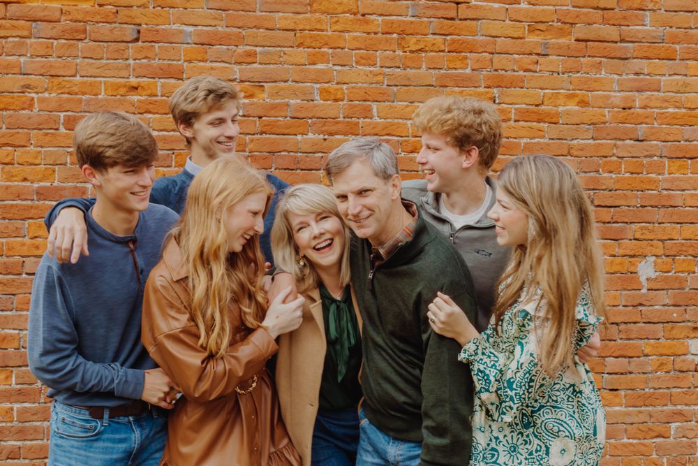 A group of young friends laughing together against a rustic brick wall background.