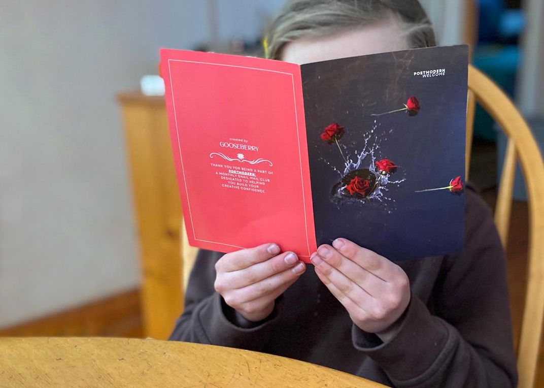 A person's hands displaying a pair of red and black hardcover books against a wooden table surface.