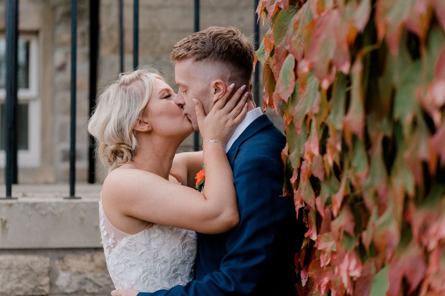 Romantic wedding couple embracing against a wall with red autumn ivy.