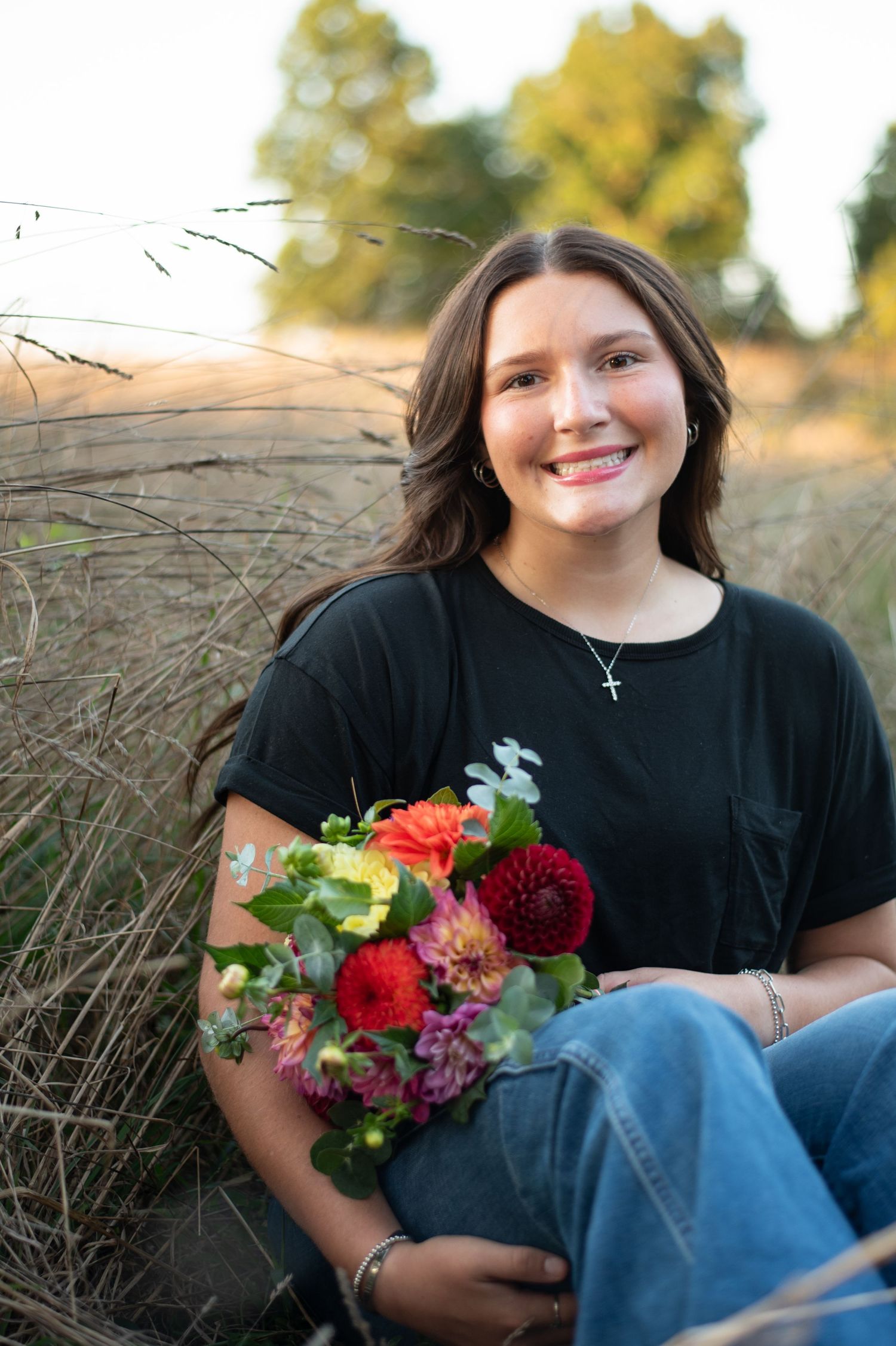 Portrait in tall grass at sunset holding colorful flower bouquet.