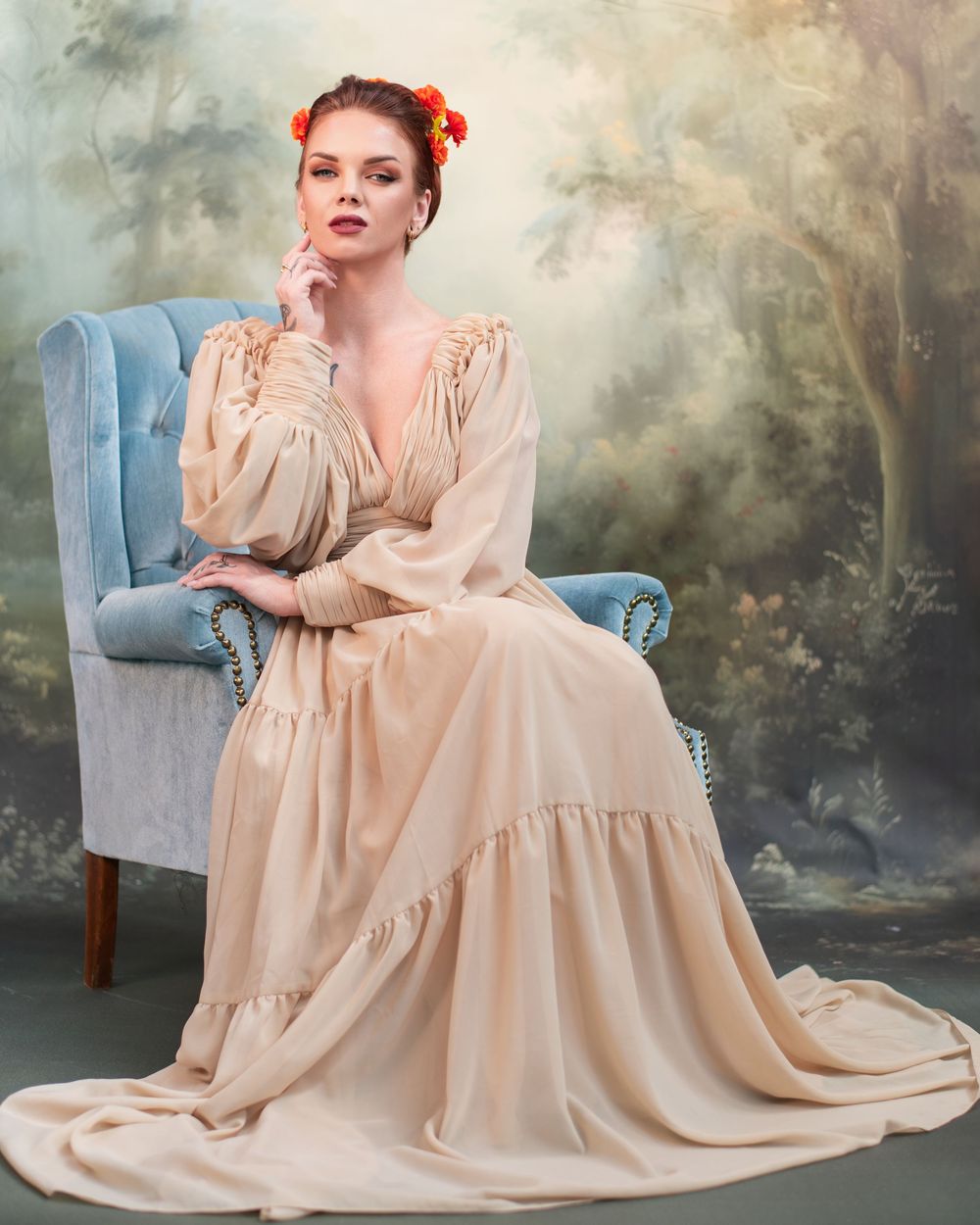 Ethereal vintage-style portrait with flowing beige dress and blue armchair against misty forest backdrop.