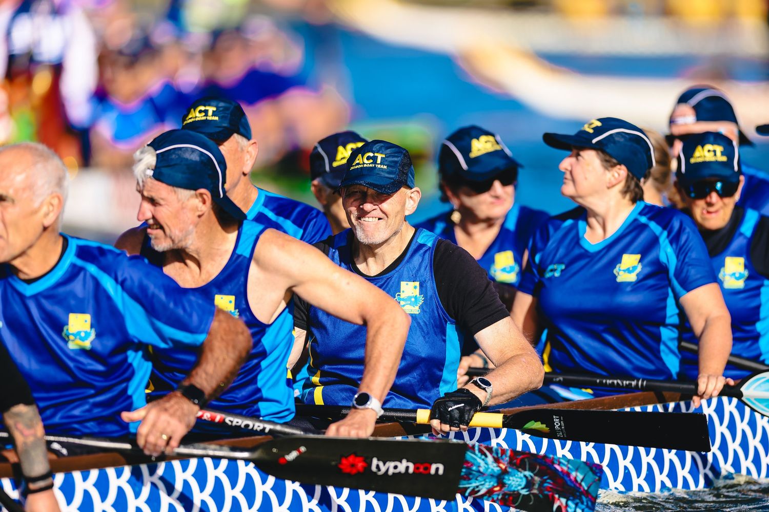 Team of dragon boat racers in yellow jerseys paddle together during competitive race event.