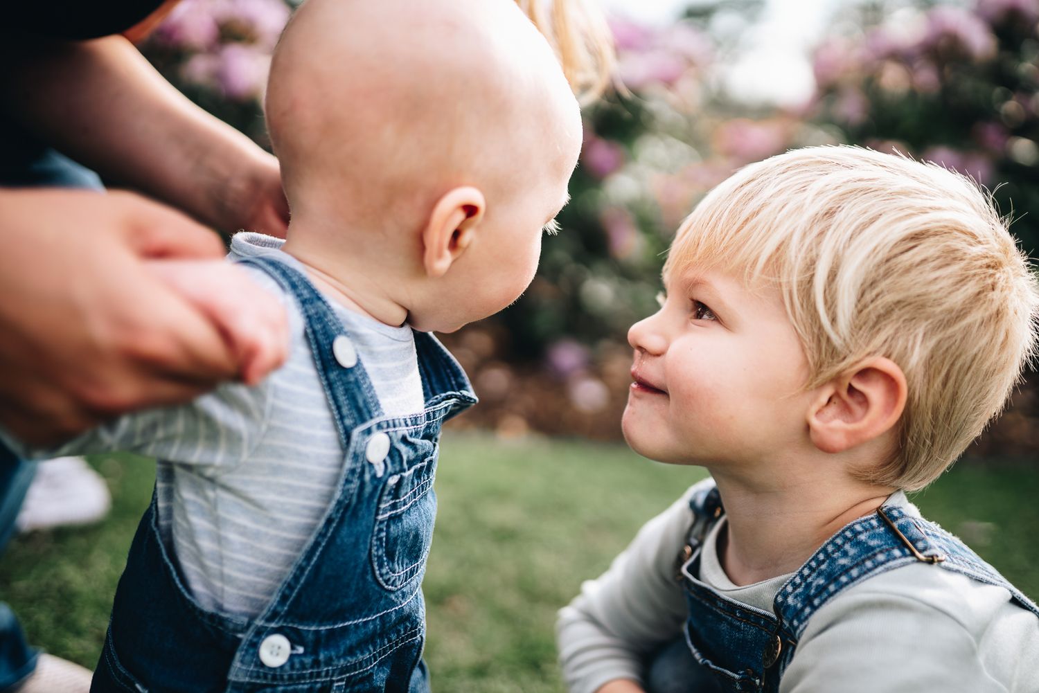 Two young children in denim outfits share a sweet moment while smiling at each other outdoors taken by Melbourne family photographer.