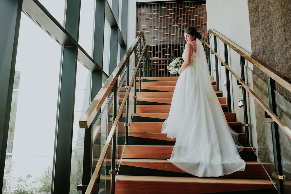 A wedding dress flows elegantly down red-carpeted stairs in a modern venue with glass walls and metal railings.