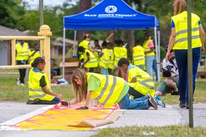 Students in safety vests work on colorful art projects spread out on blankets during an outdoor learning activity.