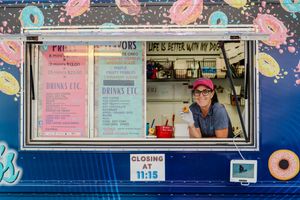 Pink and blue donut decorations adorn a retail storefront window display with posted signs and menus.