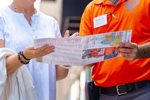 People in orange shirts and white clothing hold up papers while participating in a group activity or meeting.