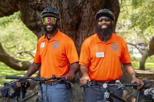 A group wearing bright orange shirts sits together outdoors under a large shady tree.