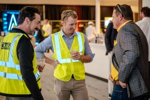 Construction workers in high visibility vests gather at a commercial building site to review project plans and documents.