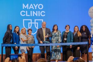 A group of people stand together on a stage at a Mayo Clinic event with blue signage in the background.