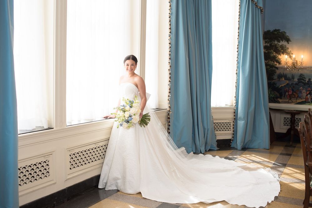 Bridal portraits by large windows with blue curtains in natural light.
