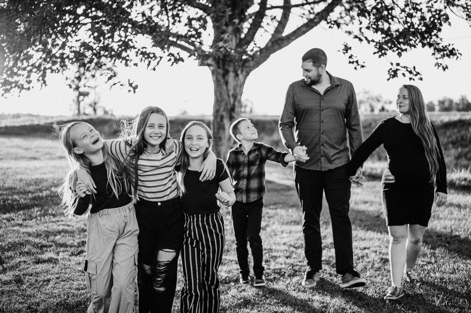 Portrait spontané en noir et blanc d’un groupe familial joyeux sous un arbre.