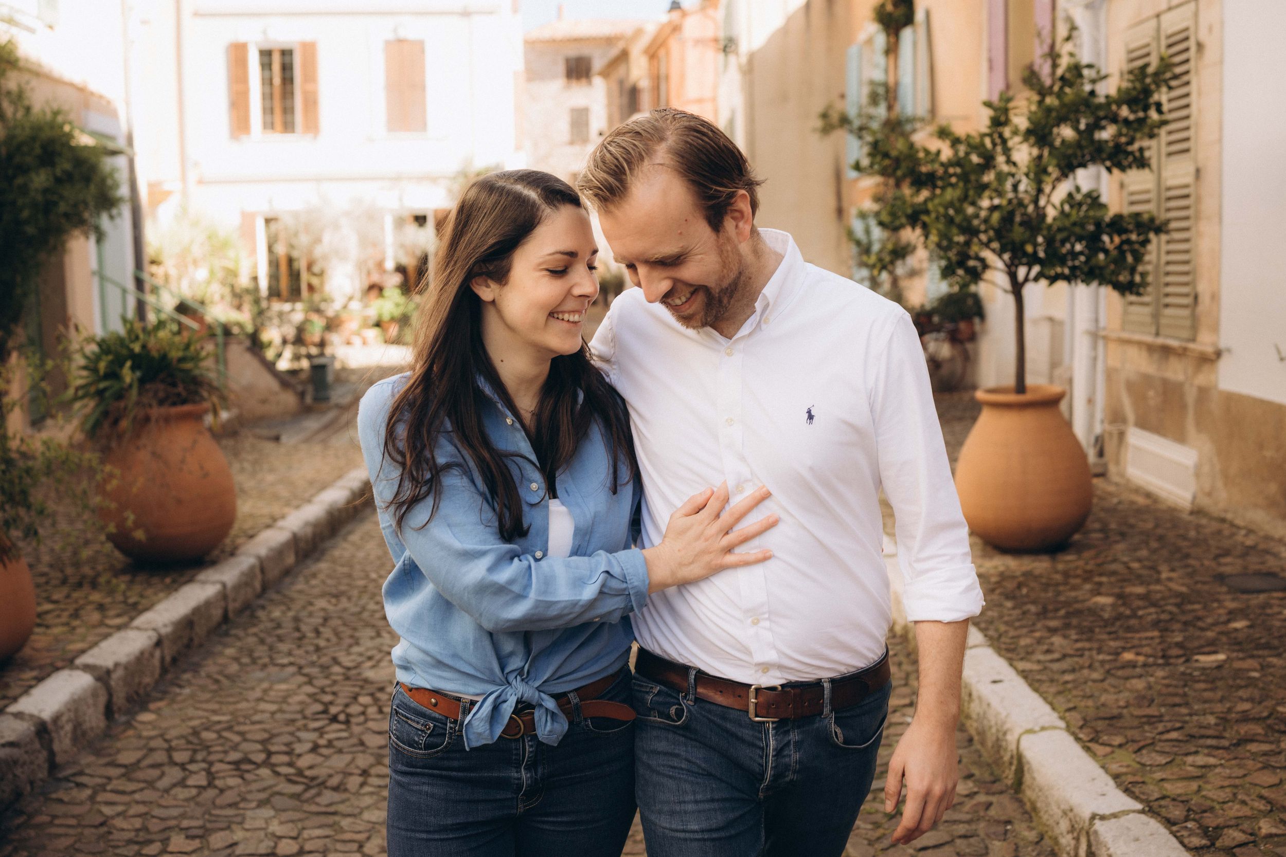 Couple smiling and embracing on a charming cobblestone street with Mediterranean architecture.