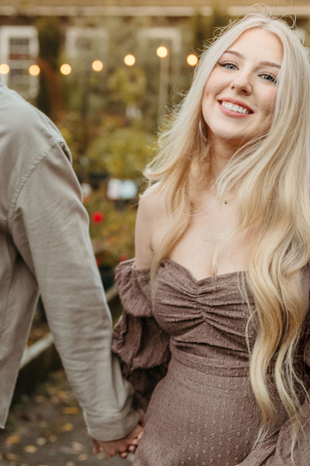 A close-up portrait showing a brown dress and blonde hair against a garden background.