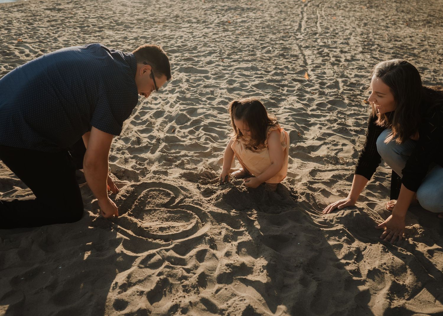 People draw in the sand together on a sunny beach during golden hour lighting creating art in the sandy surface.