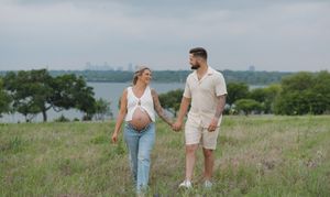 A couple enjoys a walk through a scenic hilltop meadow overlooking a lake on a summer afternoon.