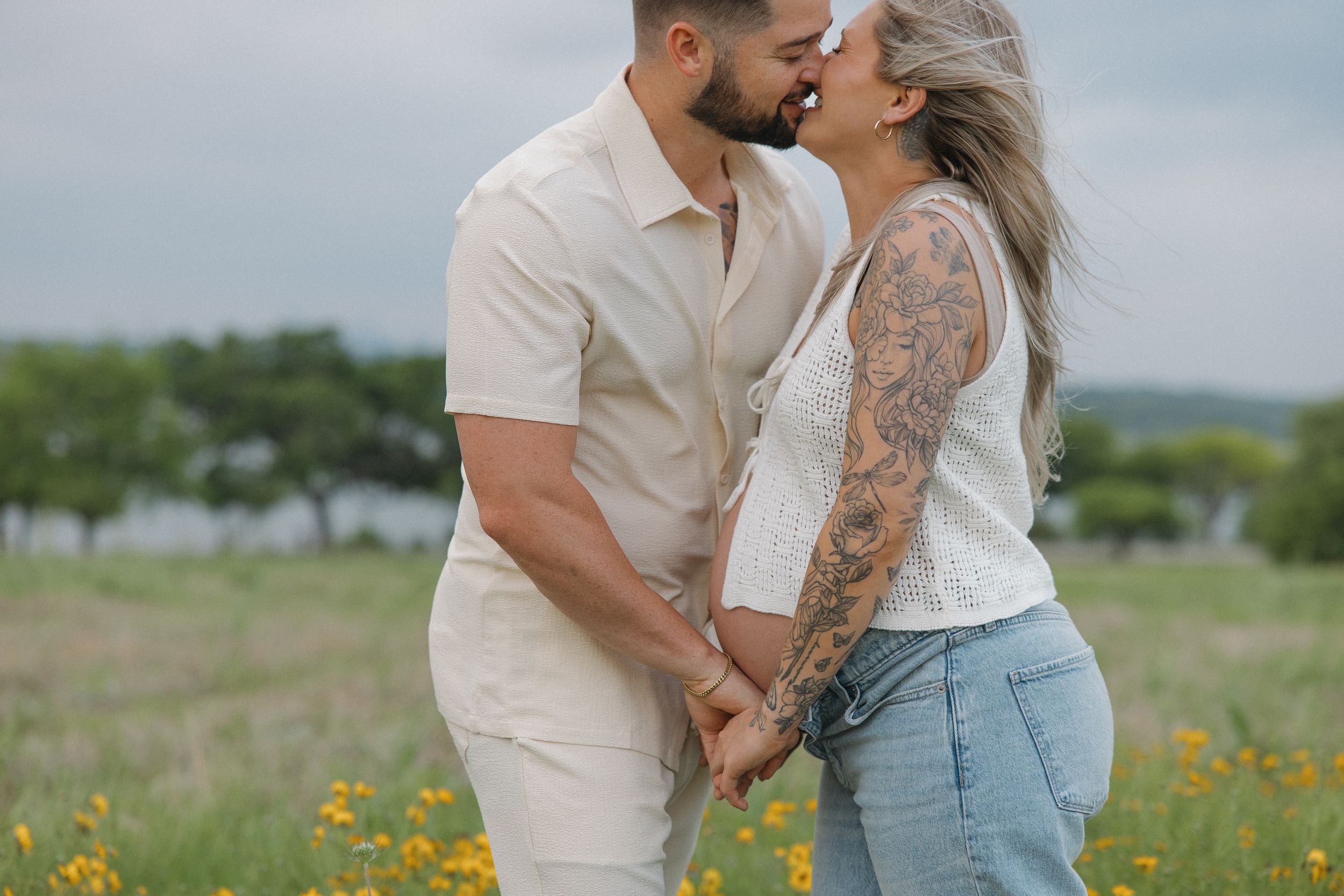 Couple holding hands in sunny meadow with yellow wildflowers, dressed in light summery outfits.