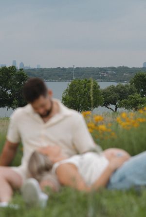 Couple relaxing on grassy hill overlooking lake and city skyline with yellow wildflowers in bloom.