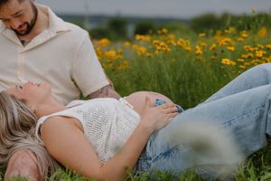 A couple relaxes together in a meadow filled with bright yellow wildflowers on a sunny day.